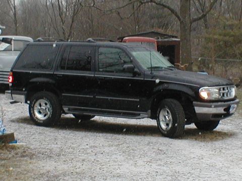 1998 Ford Taurus - A black SUV is parked on a gravel surface during a snowfall. Another vehicle is visible to the left.