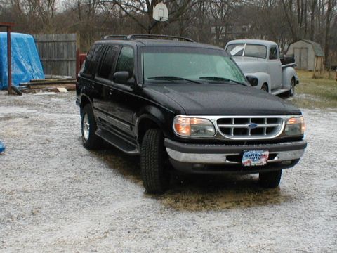 1998 Ford Taurus - A black 1998 Ford Explorer is parked in a gravel lot with a vintage pickup truck behind it.
