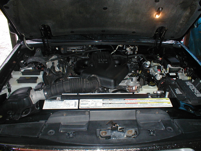 Open engine bay of a Ford truck or SUV showing intake, air box, battery and underhood label