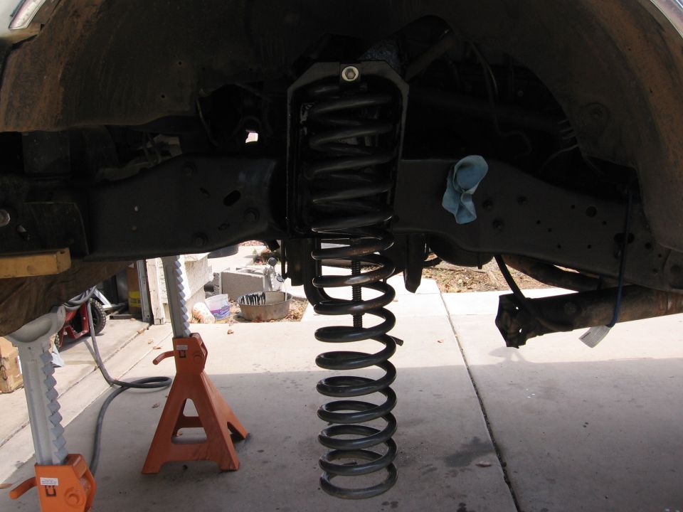 Suspension spring hanging from vehicle chassis supported by jack stands