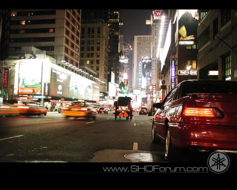 1992 Ford Taurus - A red sedan is parked on a street in a busy city at night, with blurred traffic and illuminated buildings.