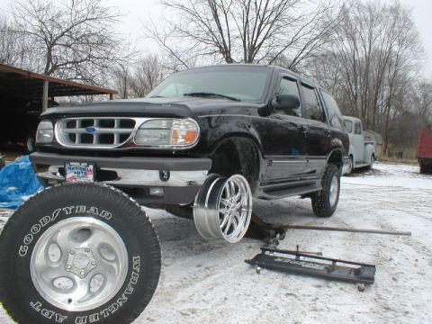 1998 Ford Taurus - A black 1998 Ford Explorer SUV is shown jacked up with one wheel removed, with other vehicles visible in the background.