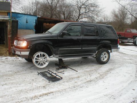 1998 Ford Taurus - SUV undergoing maintenance in a snowy environment, with a red truck parked nearby.