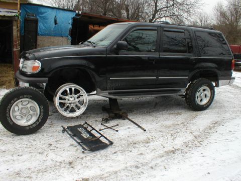 1998 Ford Taurus - A black Ford Explorer is being worked on, with one wheel removed and a jack supporting the vehicle.