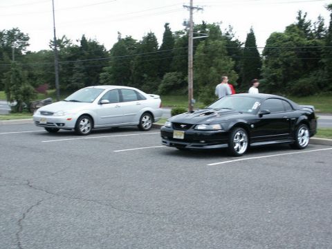 2001 Mercury Grand Marquis - A black 2001 Ford Mustang is parked in a lot, with a silver sedan visible to its left.
