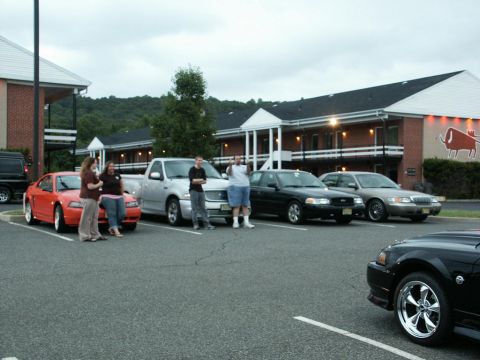 2001 Mercury Grand Marquis - People gather around cars parked in a motel parking lot on an overcast day.
