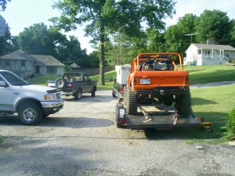 1994 Ford Bronco - An orange off-road vehicle is loaded onto a trailer, with other vehicles visible in the driveway.
