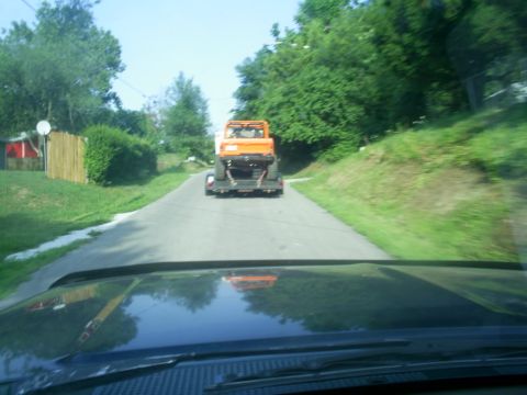 1994 Ford Bronco - An orange vehicle is being towed on a trailer down a rural road.
