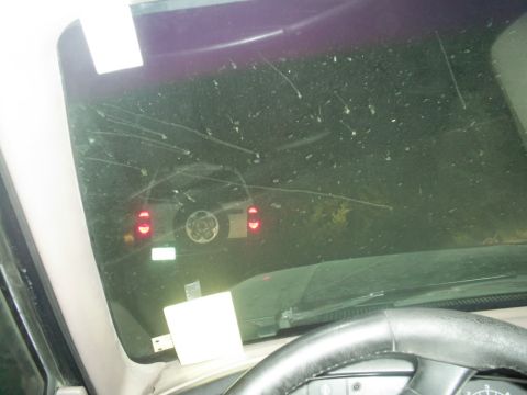 1994 Ford Bronco - View of a dark SUV from inside another vehicle, showing its rear and spare tire through a scratched and dirty windshield.