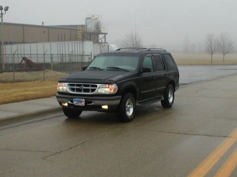 1998 Ford Taurus - This black SUV is seen from a 3/4 front angle on a wet road. The license plate is readable.