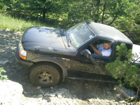 1994 Ford Bronco - A black Ford Ranger pickup truck navigates a rough, off-road terrain with a driver behind the wheel.