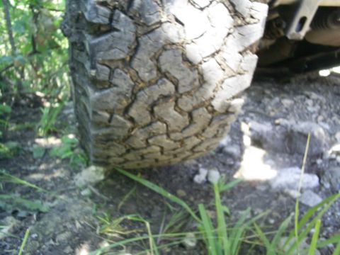 1994 Ford Bronco - A close-up view of a off-road tire, showing its tread pattern against a backdrop of dirt and grass.