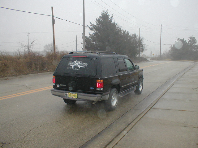 Black SUV with a sticker on the rear window driving on a wet road