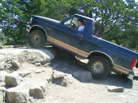 1994 Ford Bronco - A dark blue Ford Bronco is shown off-roading over rocks.