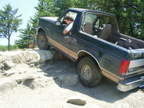 1994 Ford Bronco - A 1994 Ford Bronco maneuvers over a challenging rock obstacle on a sunny day.