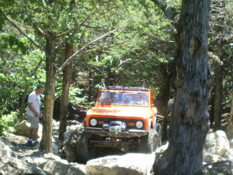 1994 Ford Bronco - Off-road vehicle tackling a challenging rocky path surrounded by trees.