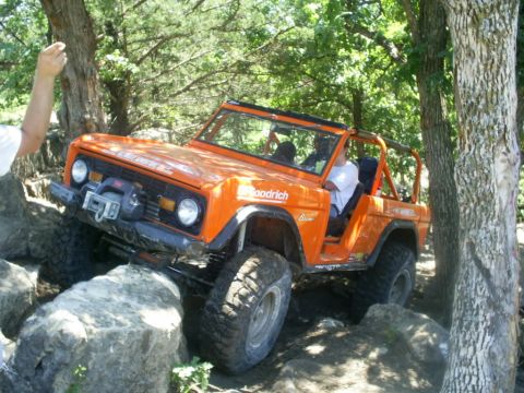 1994 Ford Bronco - This modified SUV is shown off-roading over large rocks on a wooded trail.