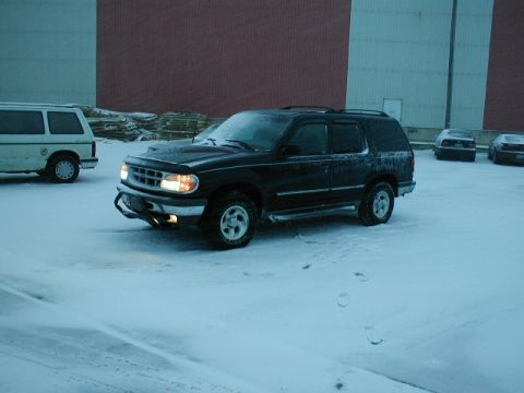1998 Ford Taurus - A black Ford Explorer is parked in a snowy lot next to a white van.