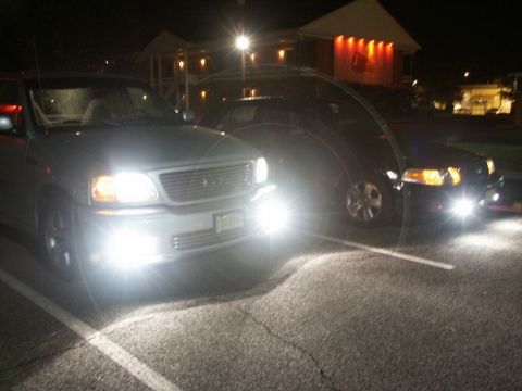 2001 Mercury Grand Marquis - A silver Ford F-150 truck is parked at night with its headlights on, alongside another dark vehicle.