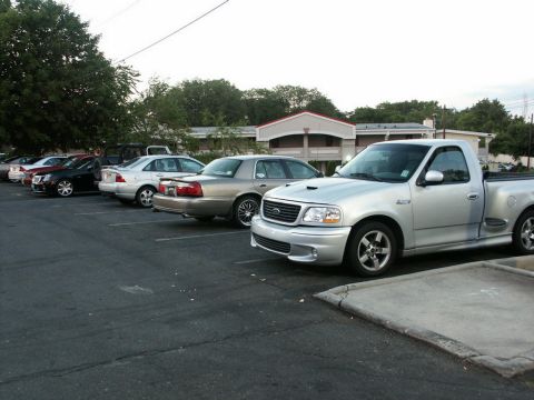 2001 Mercury Grand Marquis - A silver pickup truck with a prominent hood scoop is parked in a lot alongside other vehicles.