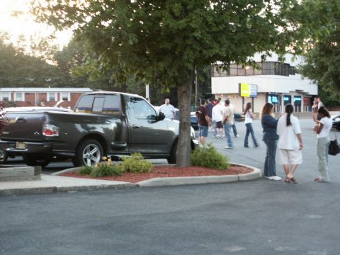 2001 Mercury Grand Marquis - A dark gray Ford F-150 pickup truck is parked under a tree at an outdoor gathering.