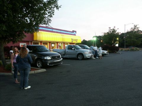 2001 Mercury Grand Marquis - A group of people stand near several trucks parked in a lot in front of a building with a yellow awning.