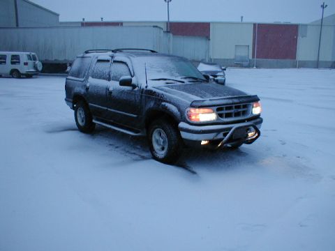 1998 Ford Taurus - A dark SUV sits covered in snow on a winter day, with a white van visible in the distance.