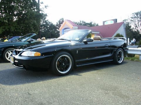 2001 Mercury Grand Marquis - A black convertible Mustang is parked outside a building with a red roof. Another car is visible to its left.
