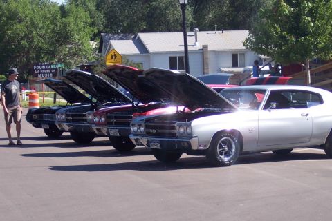 1972 Ford Ranchero - A row of classic cars, including a silver 1970 Chevrolet Chevelle SS, are displayed with their hoods open at an outdoor event.