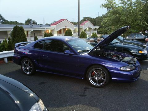 2001 Mercury Grand Marquis - A purple 1994 Ford Mustang coupe is displayed with its hood open at a car meet, alongside other vehicles.
