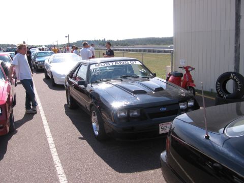 1989 Ford Mustang - A black 1989 Ford Mustang GT is parked in a line of cars, possibly at a track event.