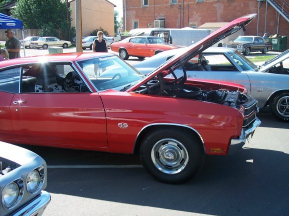 Red muscle car with hood open, parked next to a silver car. SS badge visible