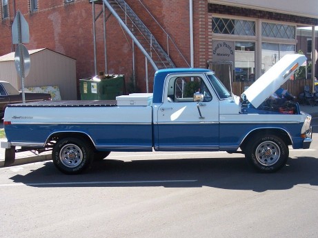 1972 Ford Ranchero - A two-tone pickup truck is parked on a street with its hood open, revealing the engine.
