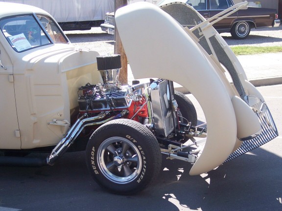 Cream-colored hot rod with hood open, showing a chrome engine and headers. Dunlop tires on chrome wheels