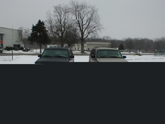 two SUVs parked in a snowy lot, one dark and one light colored
