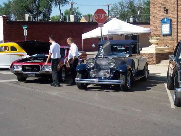 dark blue vintage convertible with hood up, parked next to a red car with hood up
