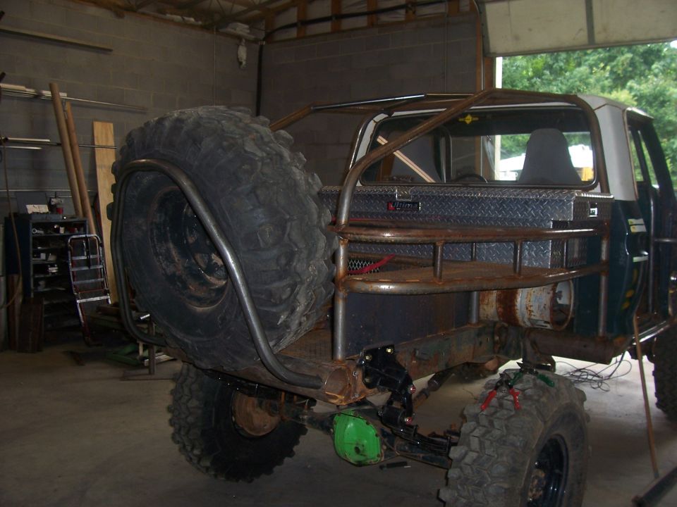 Rear of a stripped lifted truck on a buggy frame with spare tire and toolbox in a shop
