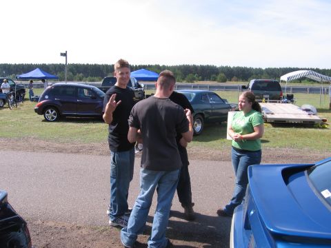 1989 Ford Mustang - People gather around vehicles at an outdoor event, with tents and trees in the background.