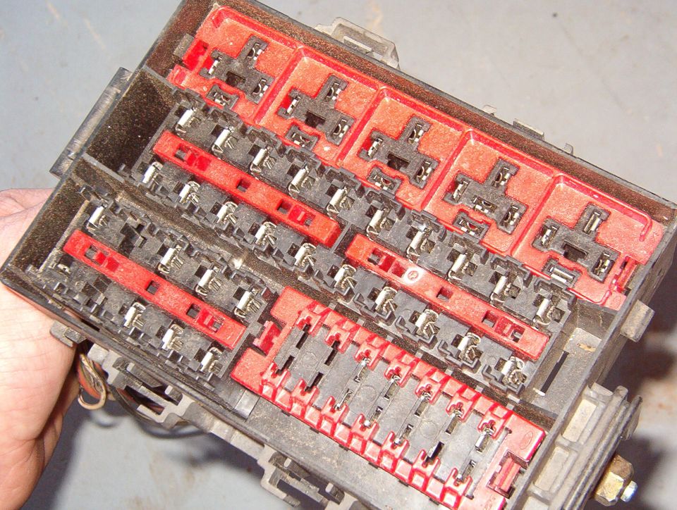 Hand holding a removed automotive fuse and relay panel with red and clear blocks