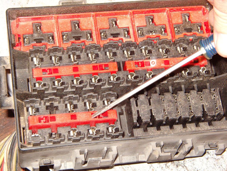 Open vehicle fuse and relay box with red bus bars being probed by a screwdriver