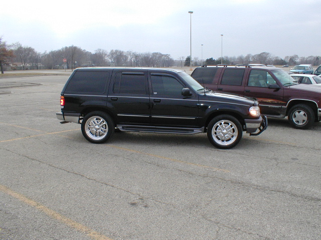 Black SUV with aftermarket wheels parked in a lot next to a maroon SUV