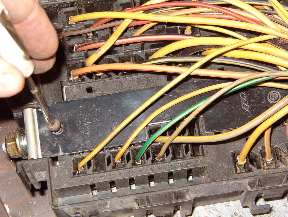 Tool desoldering a stud terminal on a fuse block buried under a tangle of yellow wires