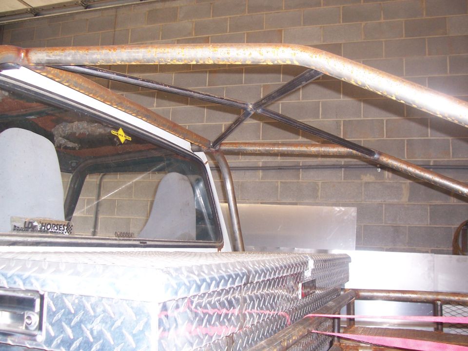 Rusty tubular roll bar arched over a pickup bed with a diamond-plate toolbox, inside a garage