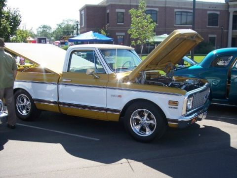 1972 Ford Ranchero - A gold and white pickup truck is parked next to a teal coupe at an outdoor event.
