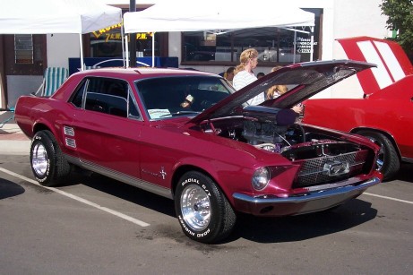 1972 Ford Ranchero - A maroon 1967 Ford Mustang coupe is parked with its hood open, revealing its engine.