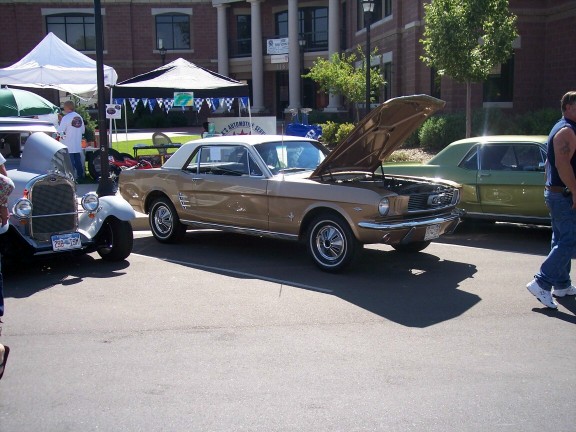 Gold 1965 Ford Mustang coupe with hood open, parked next to a silver antique car and a green sedan