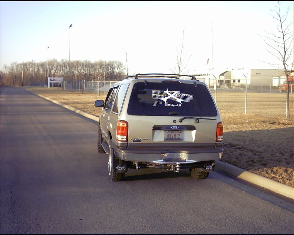 Rear of a tan Ford Explorer with dual exhaust and decal on the lift glass in a parking lot