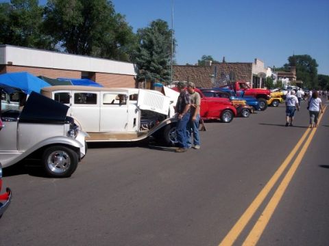 1972 Ford Ranchero - A row of classic cars are displayed on a street, with one white sedan having its hood open for viewing.