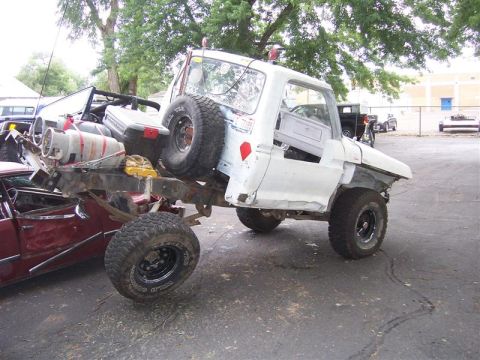 1978 Ford Bronco - Modified pickup truck chassis loaded with equipment, partially obscuring another vehicle.