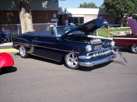 1972 Ford Ranchero - A dark blue convertible is parked with its hood open, its engine bay at an outdoor event.